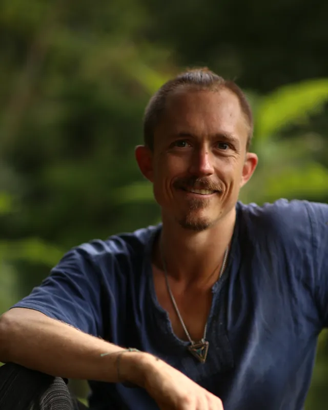 Ryan Murphy smiling, leaning on a tree in the forest.